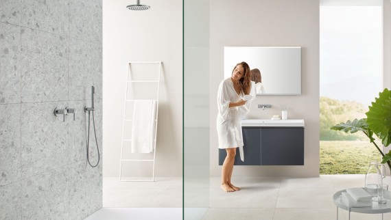 Woman drying her hair with a towel in a bathroom with open shower and large tiles in terrazzo style