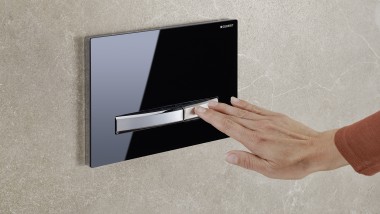 A hand activates the flush on a black Sigma50 actuator plate (© Geberit)