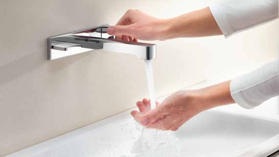 Macro image with hands turning a Geberit ONE tap and checking the water flow and temperature