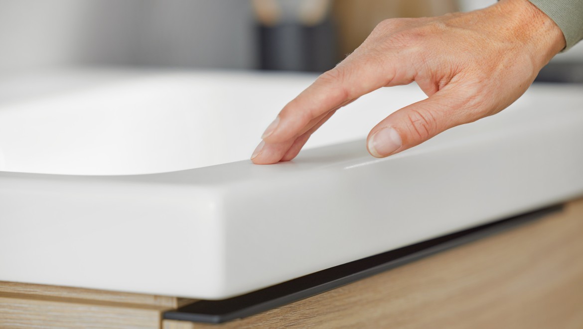 Macro image of a hand touching a Geberit iCon washbasin in white matt