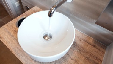 Water flows out of the Geberit Piave wall-mounted tap into a VariForm lay-on washbasin